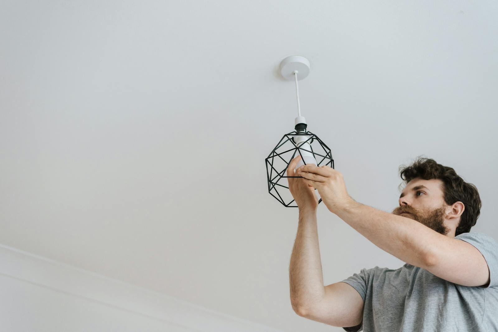 Electricista Lauzier San Juan Alicante A professional electrician skillfully installing a modern geometric ceiling lamp indoors.